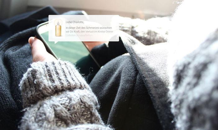 Nahaufnahme eines Handys in einer Hand, umgeben von einem grauen Pullover und einer schwarzen Jacke.